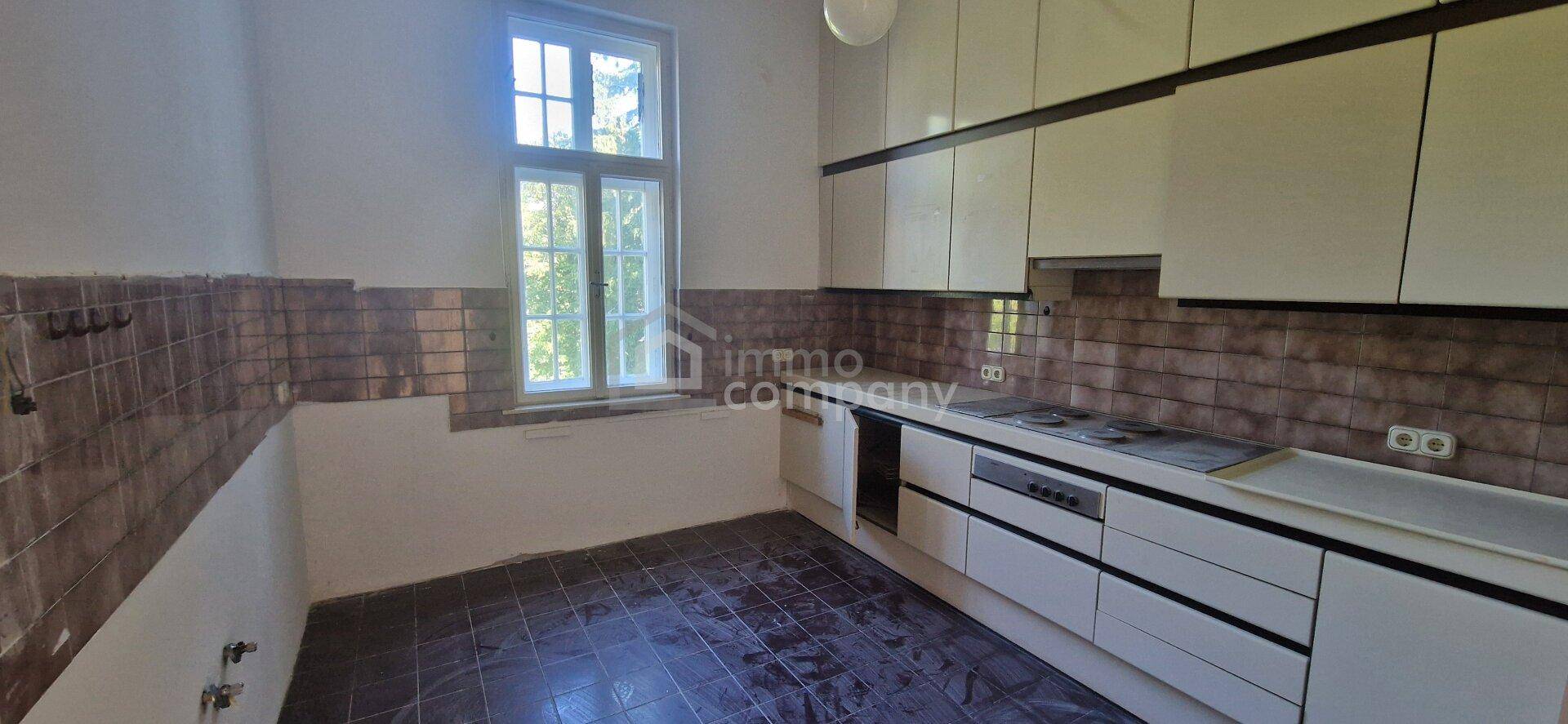 Küche mit Einbauschränken, Fliesenboden und Fenster, die eine Modernisierung benötigt.