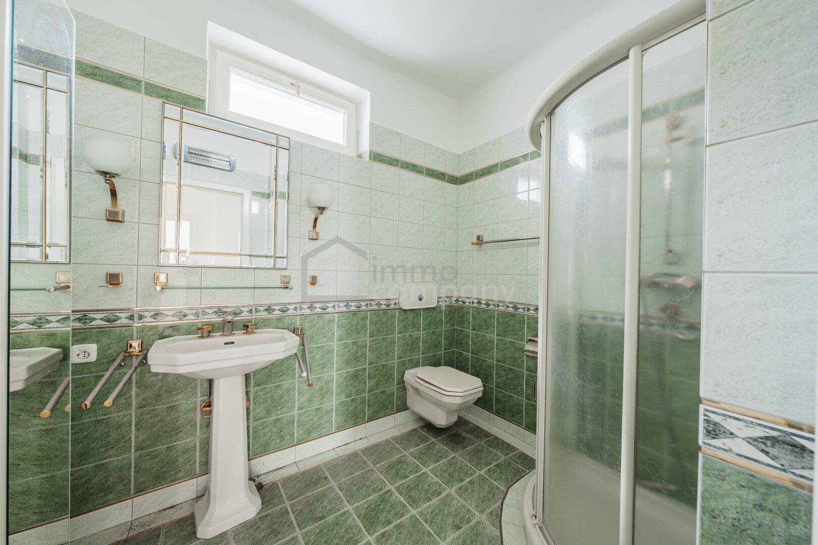 Badezimmer mit grünen Fliesen, Duschkabine, Standwaschbecken und Fenster für Tageslicht.