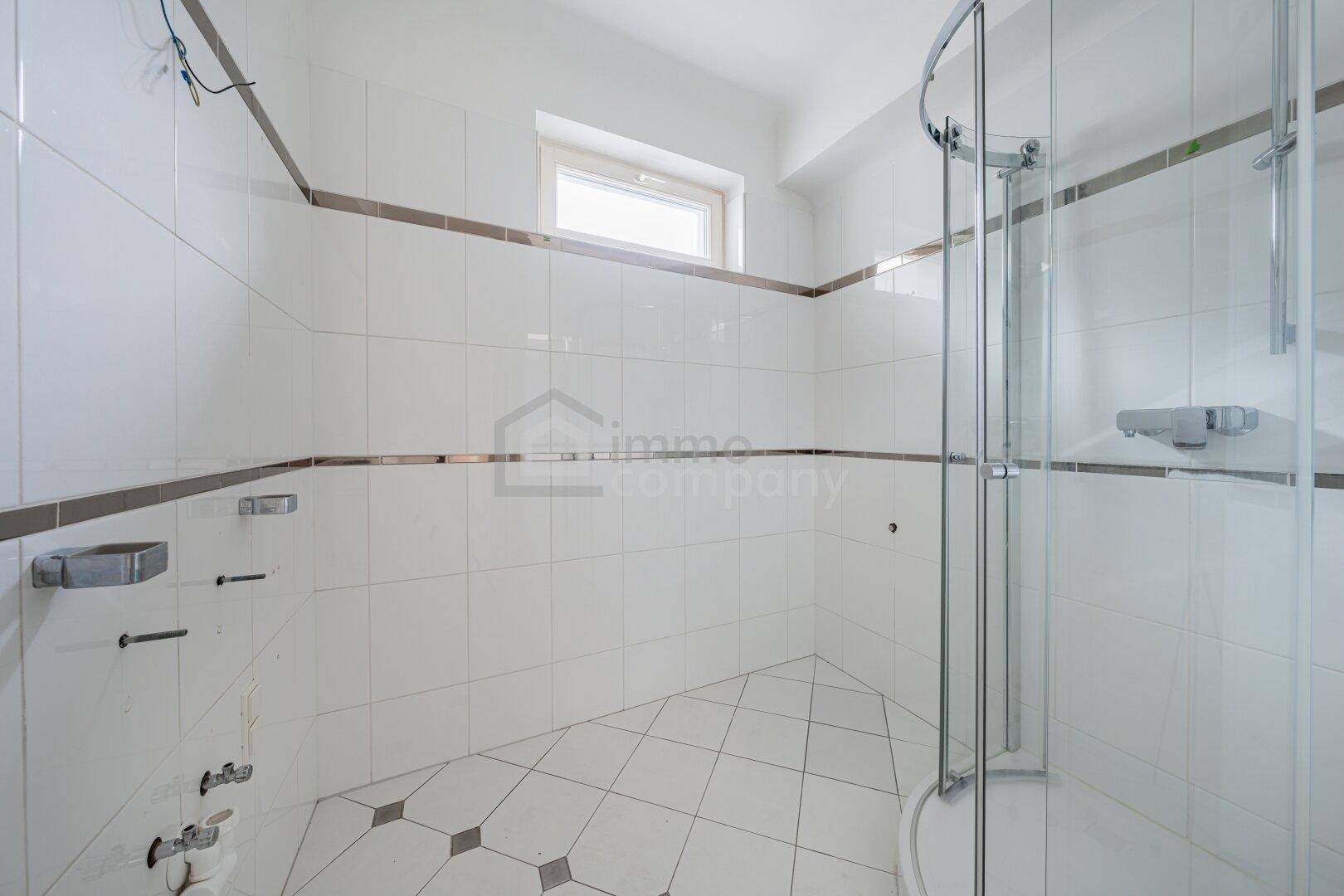 Modernes Badezimmer mit weißen Fliesen, Duschkabine und Fenster für natürliche Belüftung.