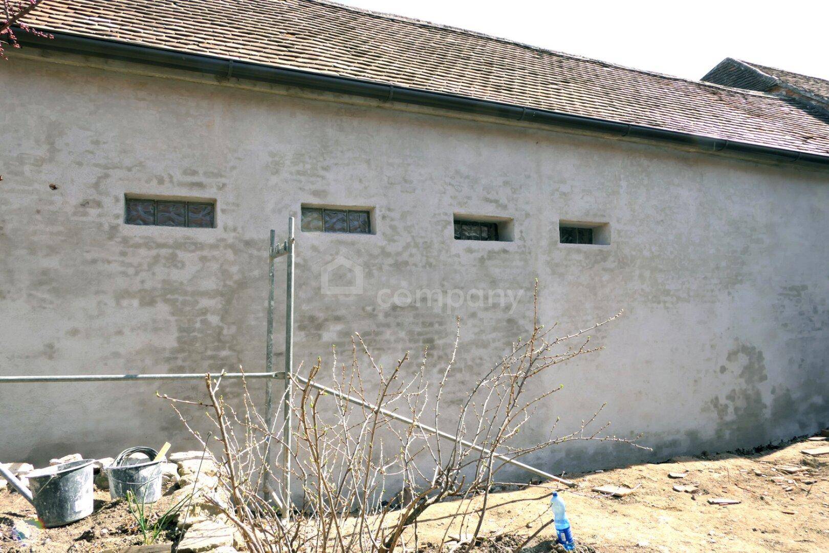 Alte Gebäudefassade mit kleinen Fenstern und Putz, der Renovierungsbedarf zeigt.