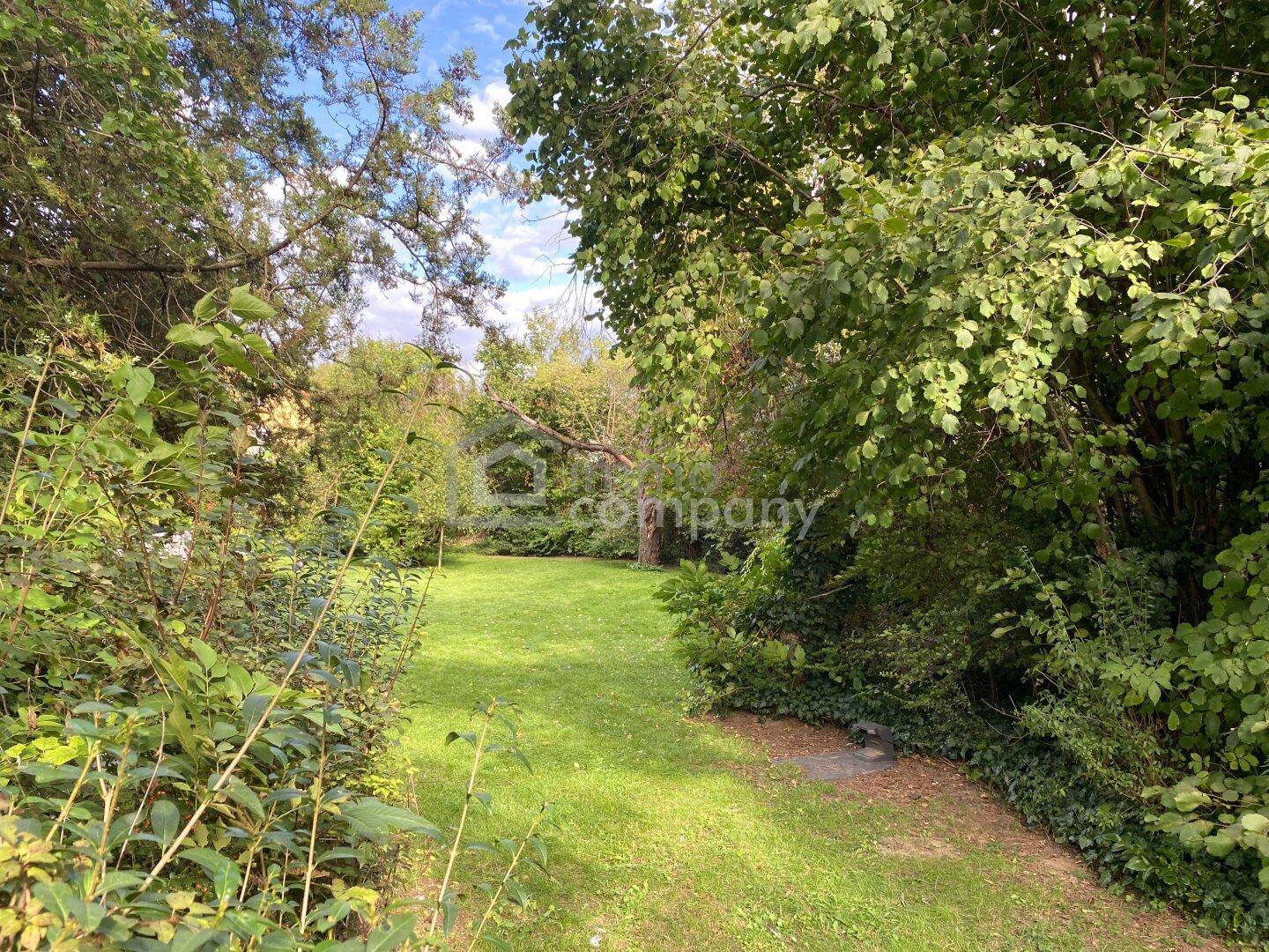 Idyllischer Gartenweg umgeben von üppigem Grün und hohen Bäumen, ideal zum Entspannen.