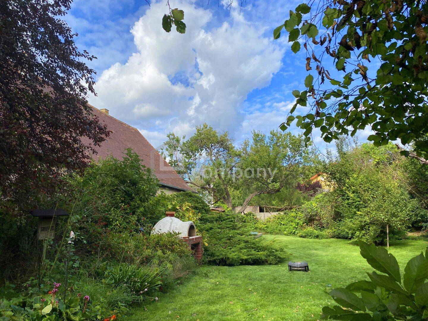 Sonniger Garten mit Rasenfläche, Pizzaofen und Blick auf das charmante Landhaus.