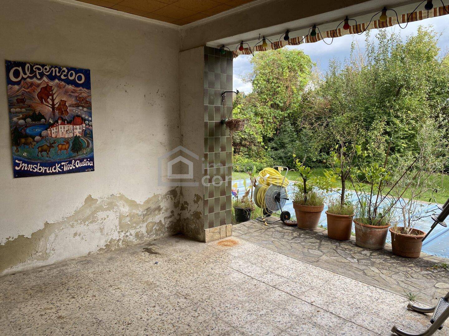 Überdachte Terrasse mit Fliesenboden und Blick in den Garten, bereit zur Gestaltung.