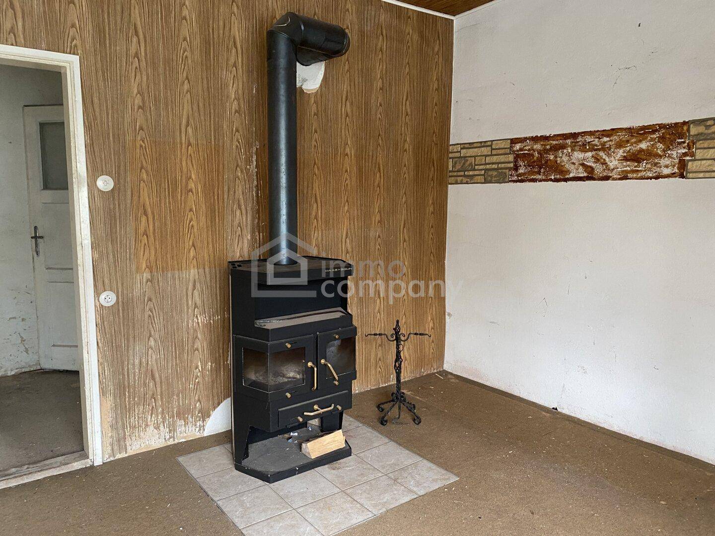 Rustikaler Raum mit einem Holzofen, Holzvertäfelung und Fliesenboden, renovierungsbedürftig.
