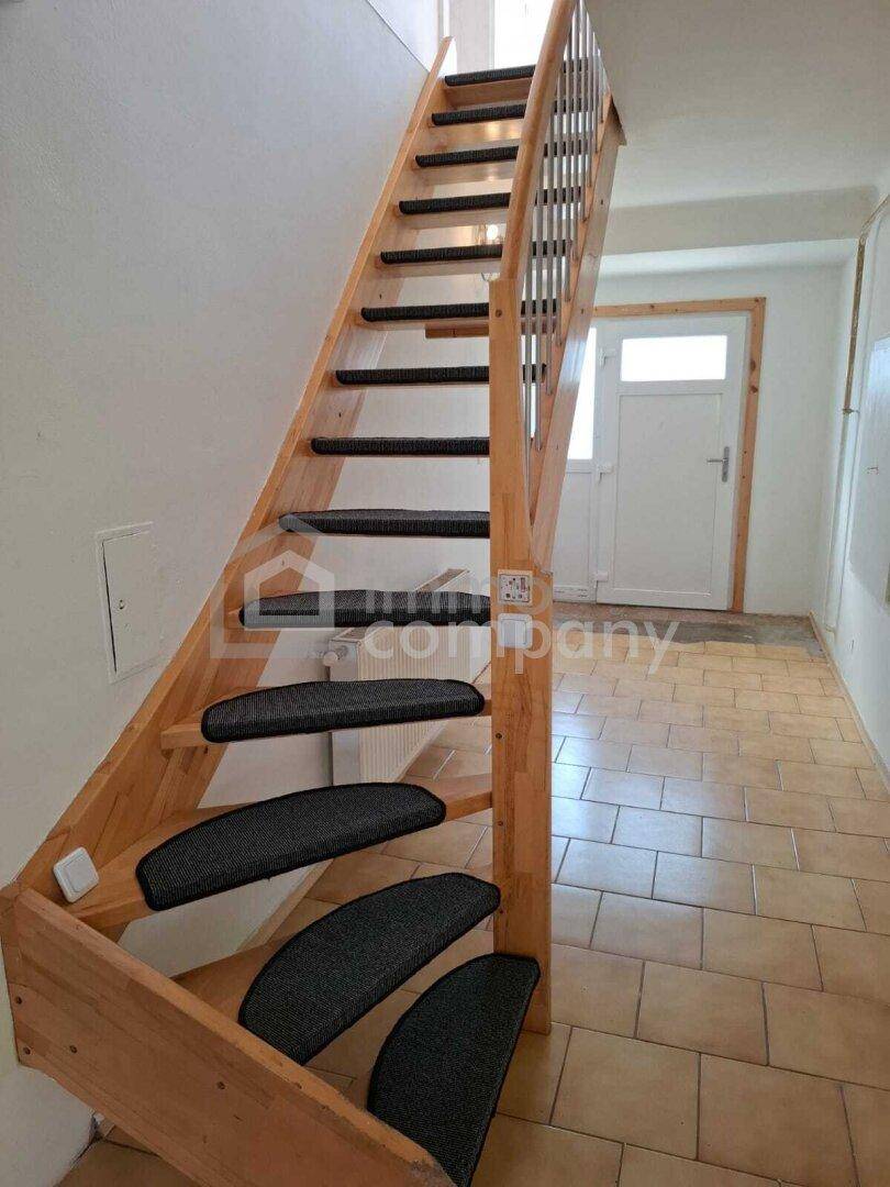 Holztreppe mit Teppichstufen führt von einem gefliesten Bereich nach oben.