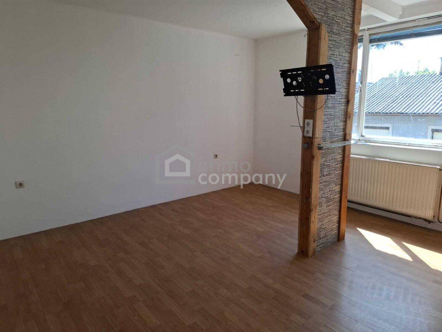 Leeres Wohnzimmer mit Laminatboden, dekorativem Steinpfeiler und Fenster.