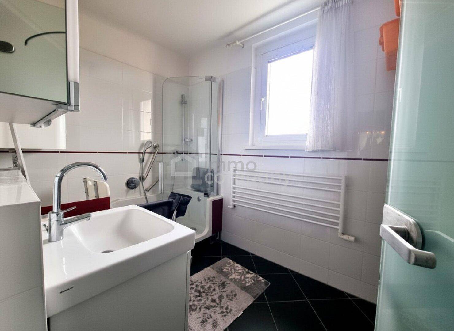 Helles Badezimmer mit Dusche, Einzelwaschbecken, Fenster und Handtuchheizkörper.