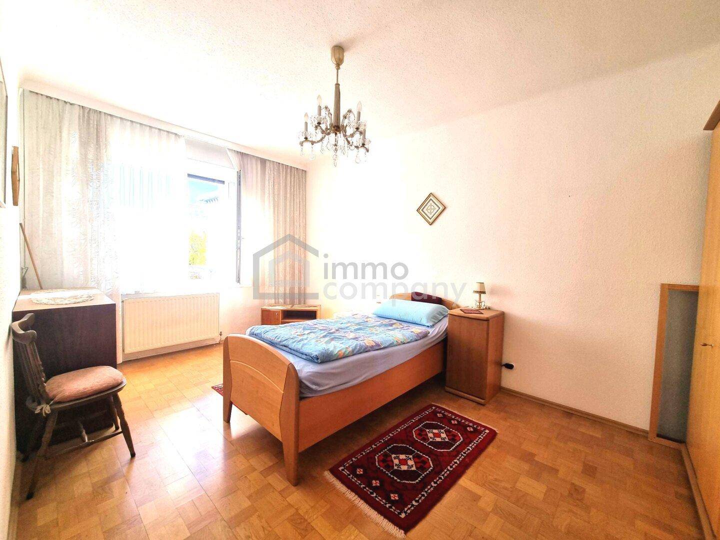 Schlafzimmer mit Einzelbett, Holzmöbeln und einem klassischen Kronleuchter.