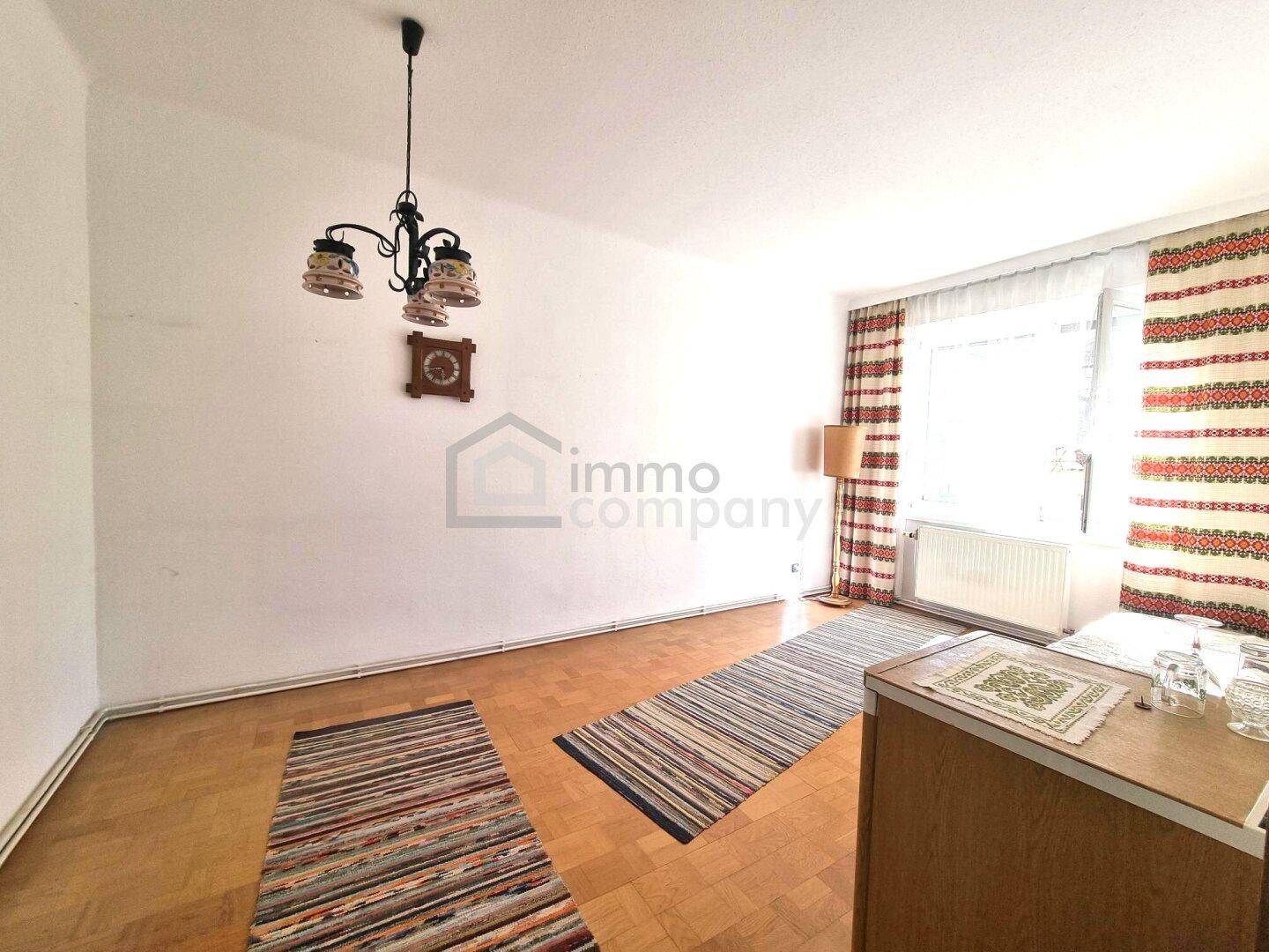 Unmöbliertes Schlafzimmer mit Parkettboden, Fenster und einem Kronleuchter.