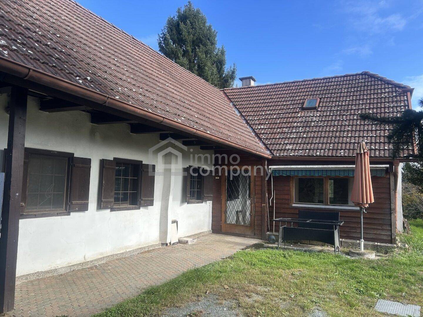 Seitenansicht des Hauses mit Eingangsbereich, Ziegeldach und angrenzender Grünfläche.