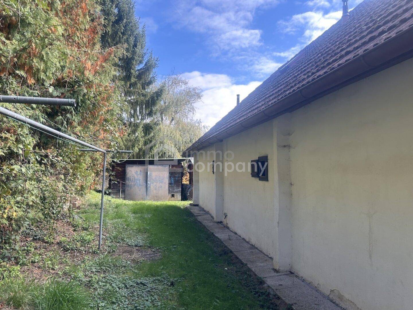 Seitenansicht des Hauses mit angrenzendem Schuppen und Wäscheständer im Gartenbereich.
