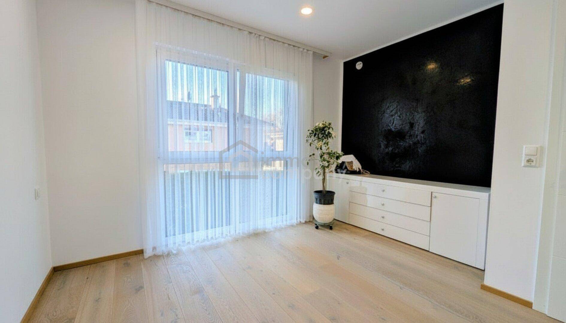 Heller Raum mit Parkettboden, großem Fenster und moderner Kommode.
