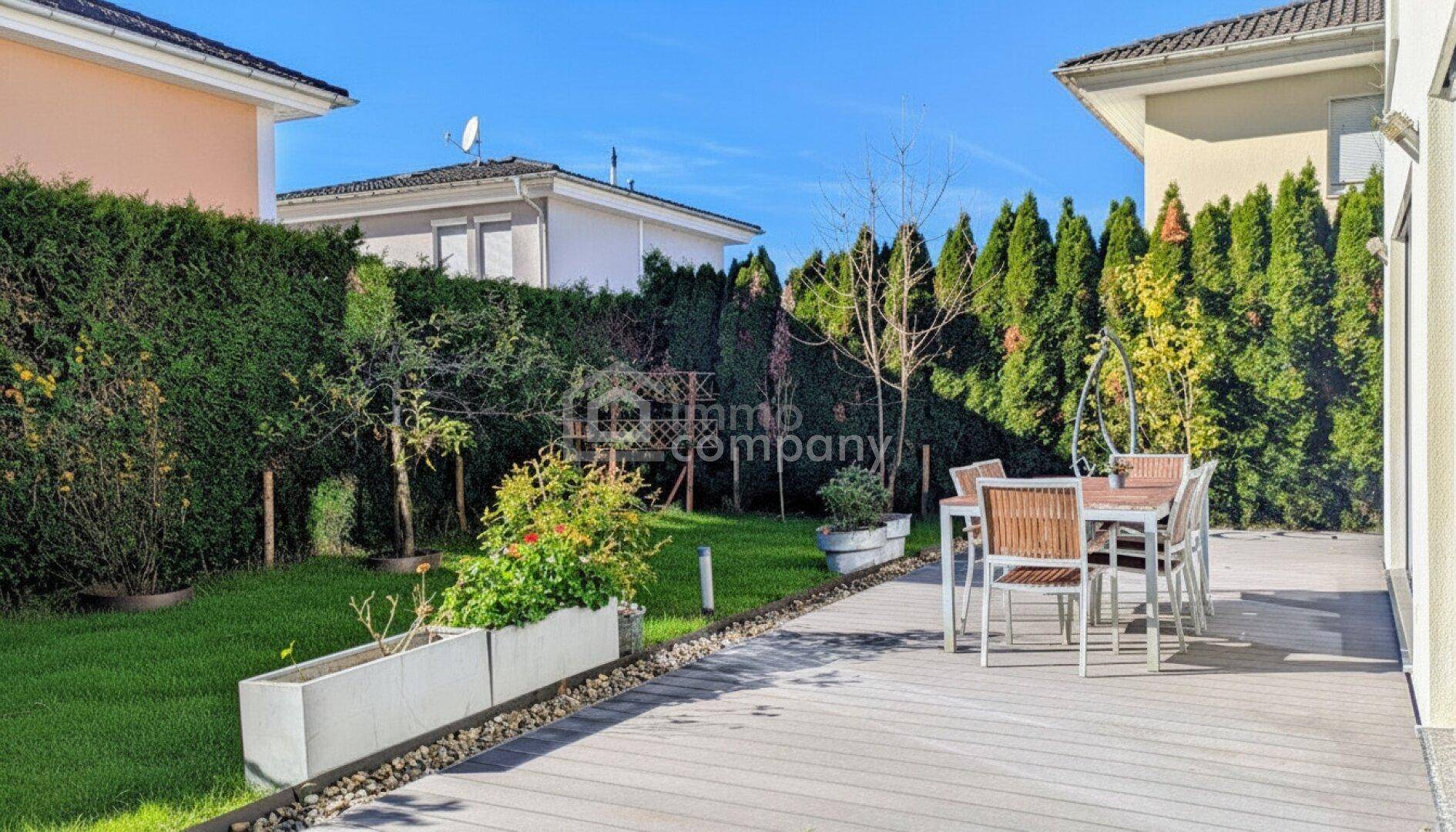 Sonniger Außenbereich mit großer Terrasse, Gartenmöbeln und gepflegter Hecke.