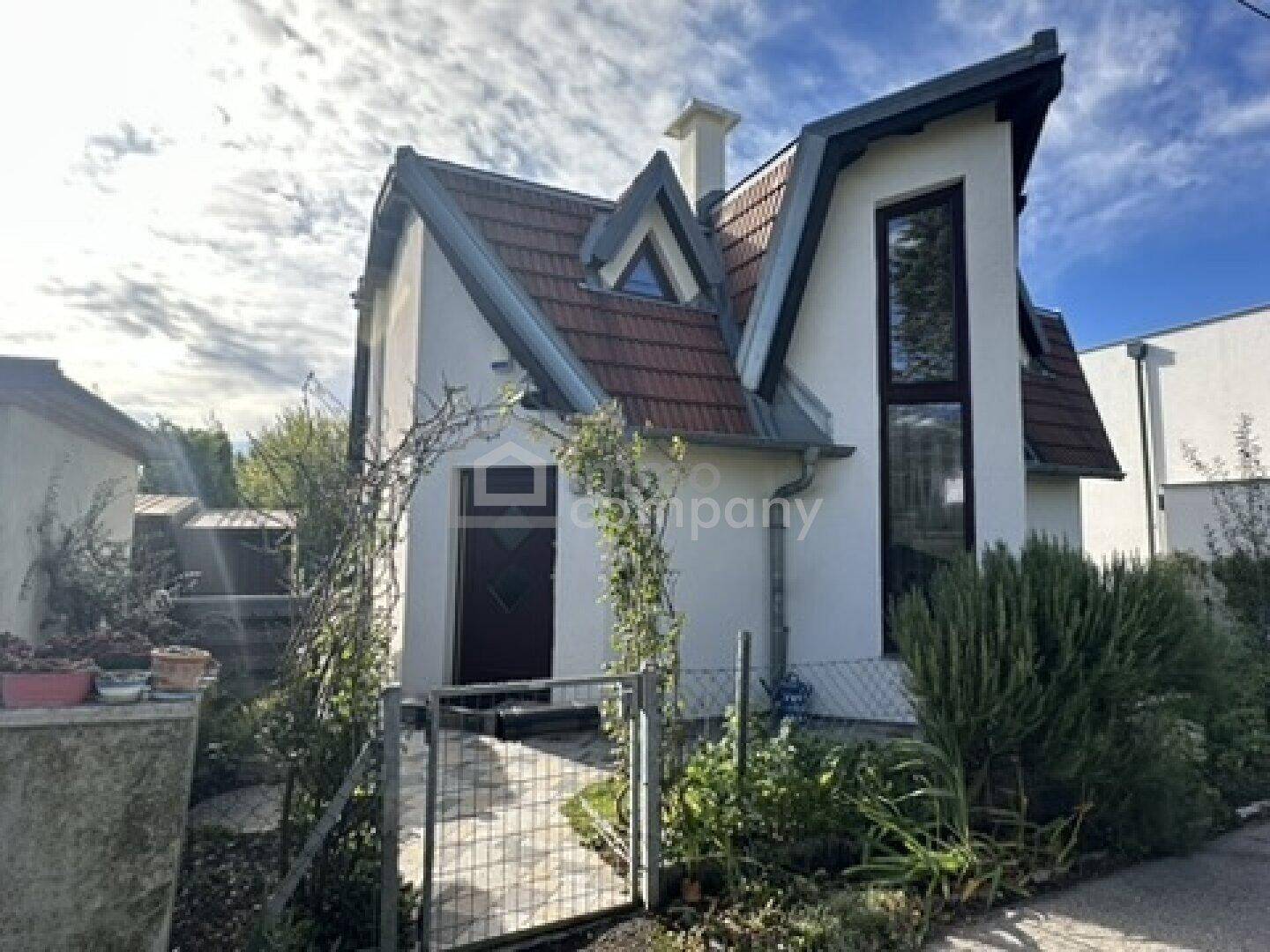 Vorderansicht des Hauses mit Eingangsbereich, Giebeldach und hohen Fenstern.