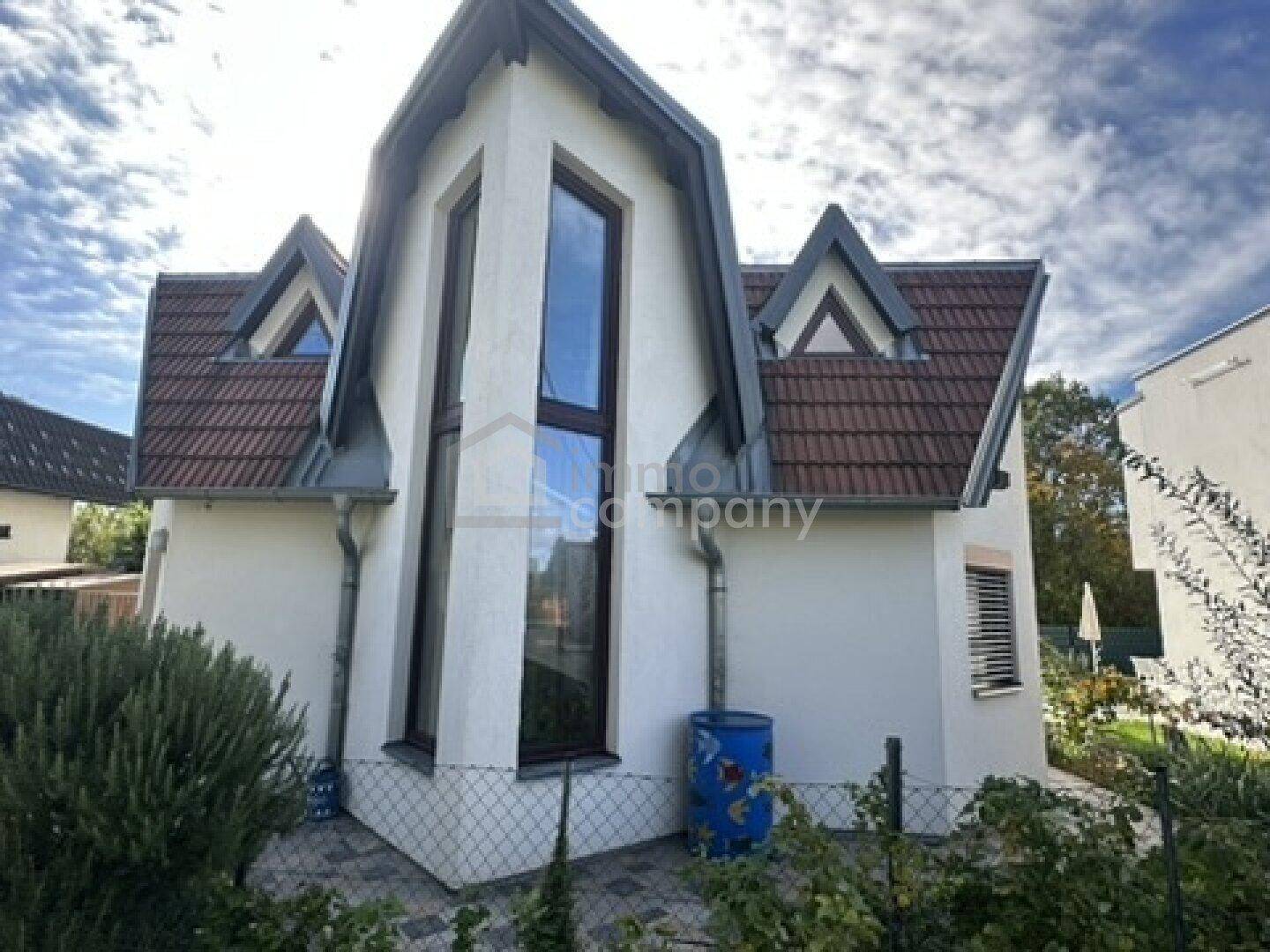 Rückansicht des Hauses mit markanten Giebelfenstern und Ziegeldach, umgeben von Grün.