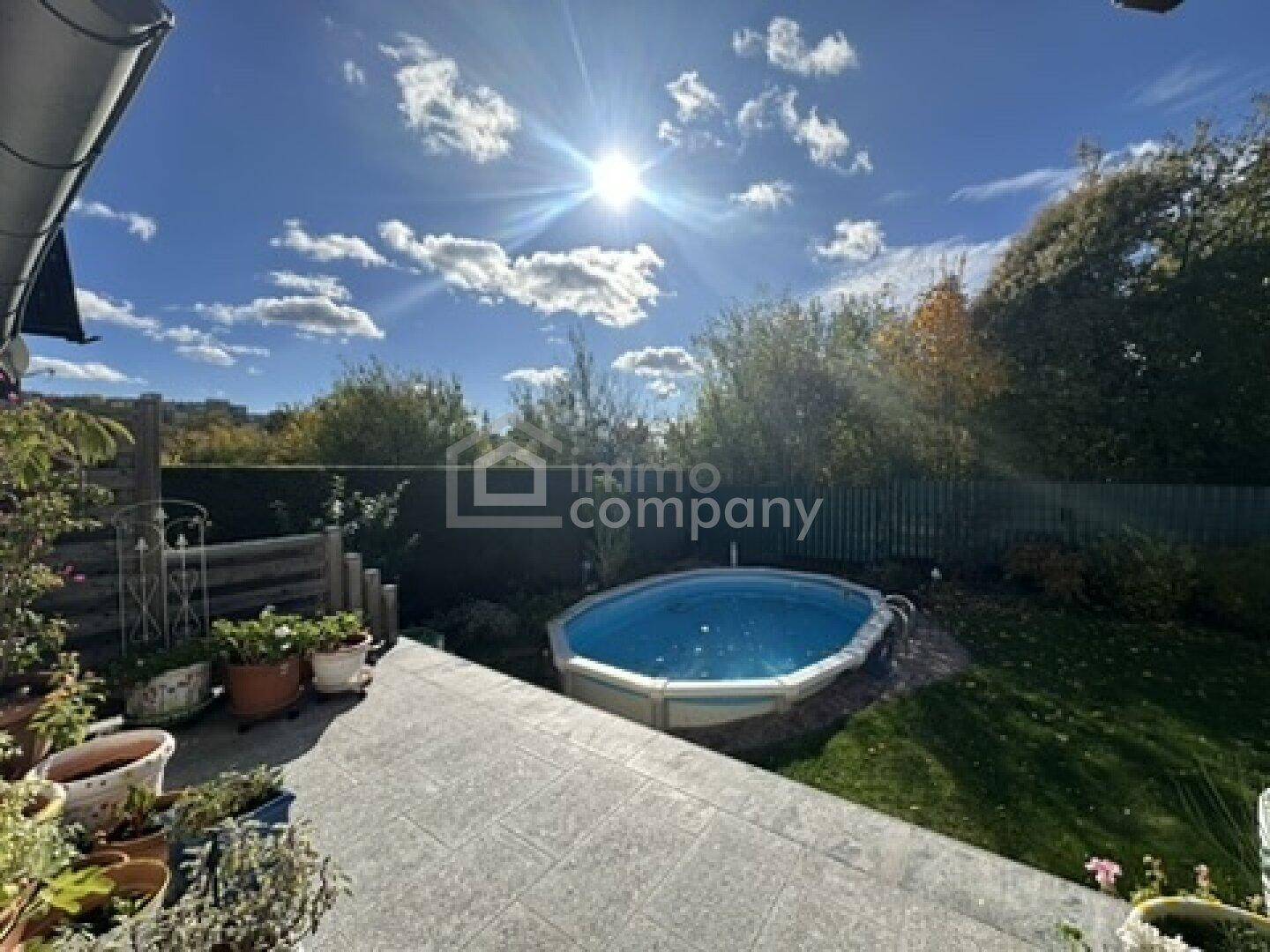 Sonniger Gartenbereich mit gepflasterter Terrasse, Rasenfläche und einem Aufstellpool.