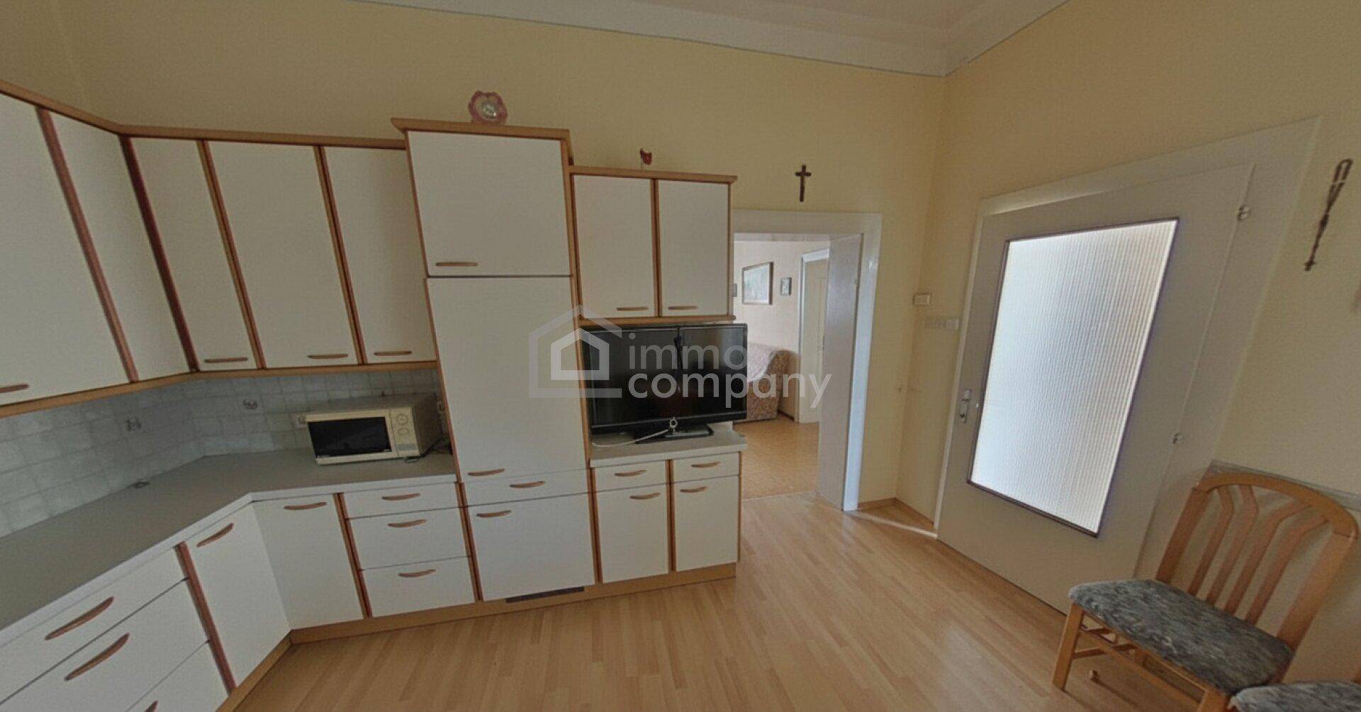 Geräumige Küche mit vielen weißen Einbauschränken, Mikrowelle und Zugang zu einem weiteren Zimmer.