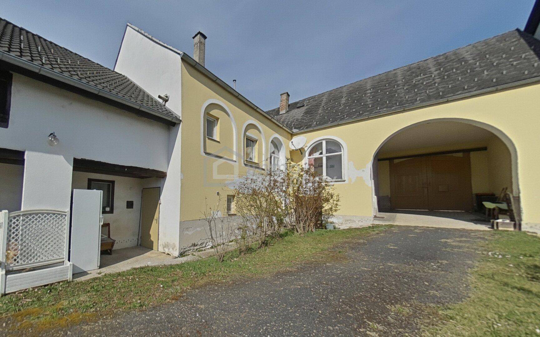 Gelbe Gebäudefassade mit einem großen Torbogen und sichtbaren Gebrauchsspuren, umgeben von einer Auffahrt.