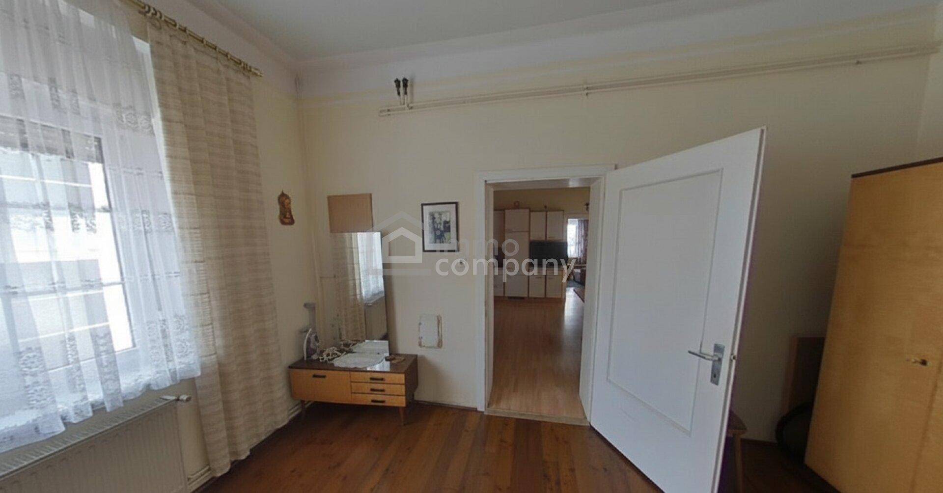 Helles Zimmer mit Holzboden, großem Fenster und einem kleinen Schminktisch mit Spiegel.