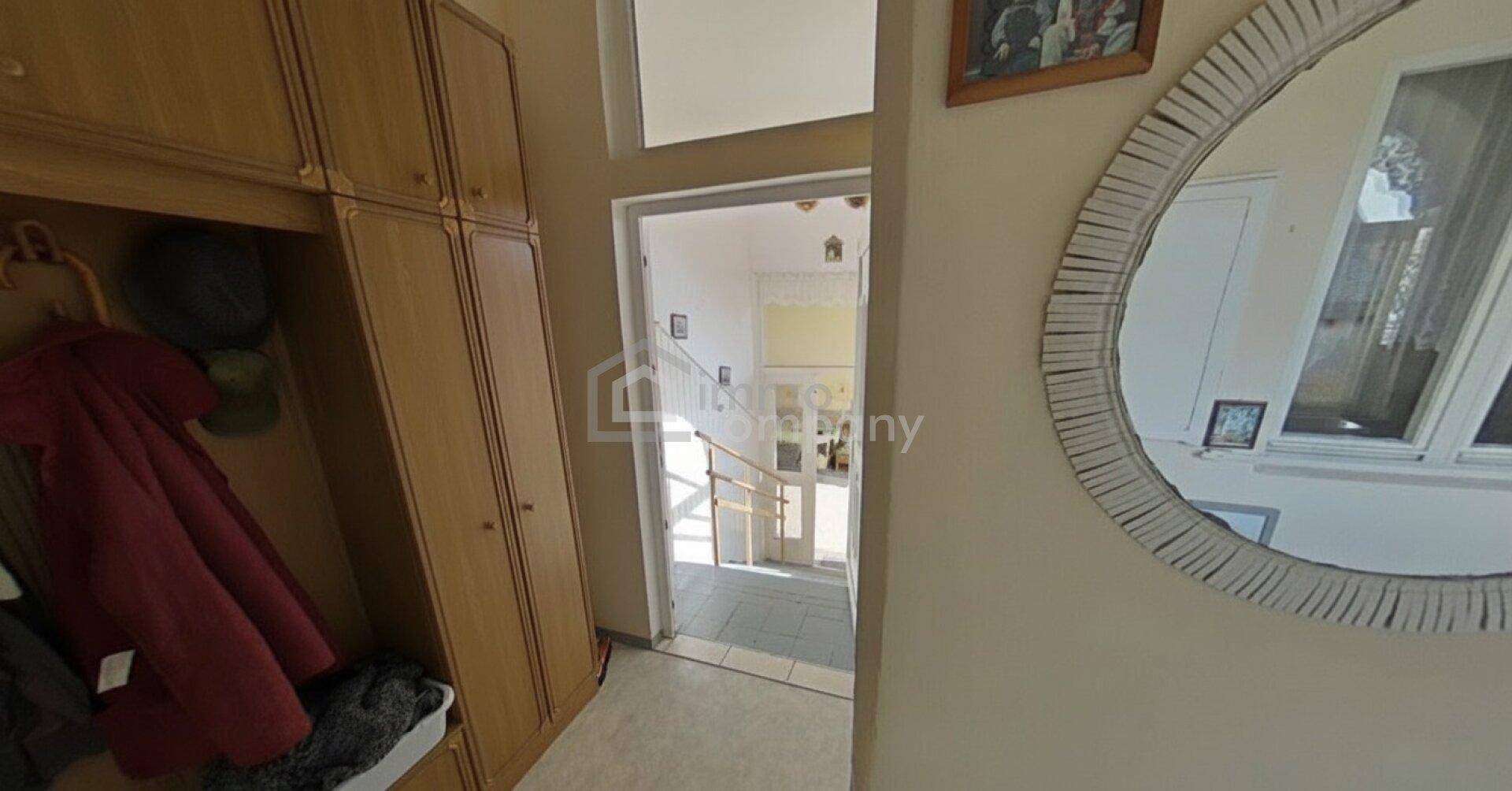 Eingangsbereich mit Holzgarderobe, rundem Spiegel und Blick auf das Treppenhaus.