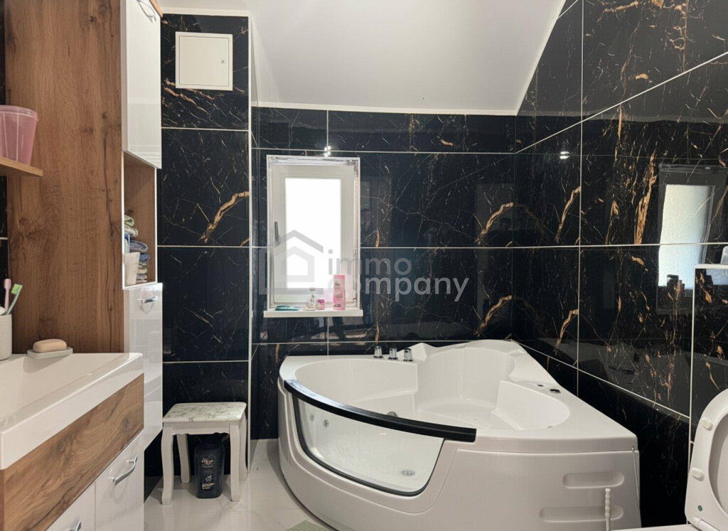 Elegantes Badezimmer mit schwarzen Marmorfliesen, moderner Eckbadewanne und Fenster.