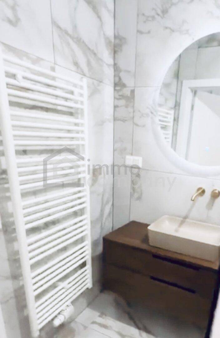 Modernes Badezimmer mit Marmorfliesen, beleuchtetem Spiegel und beheiztem Handtuchhalter.
