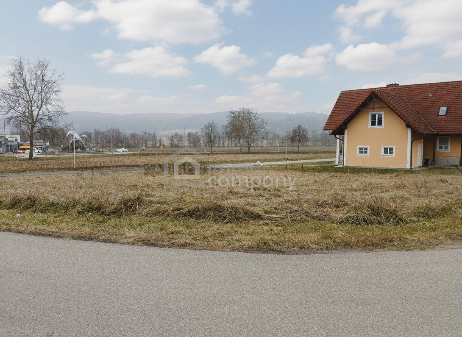 Freies Grundstück neben einem gelben Wohnhaus mit Blick auf eine weite Landschaft und bewaldete Hügel.