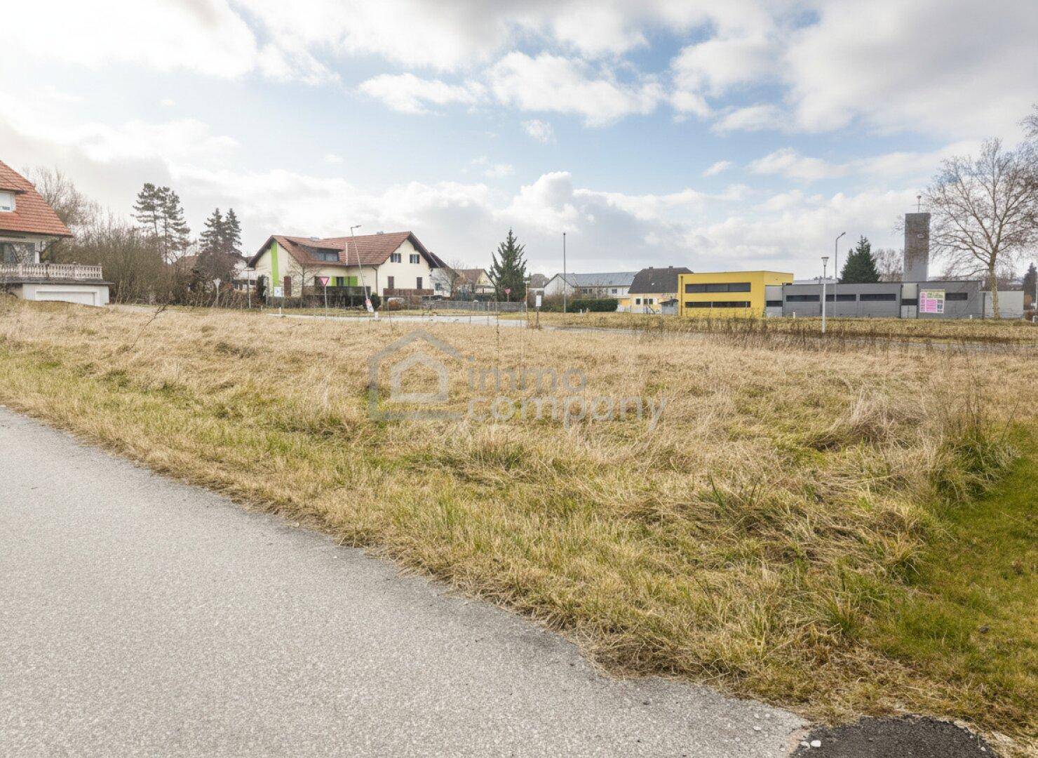 Offenes Feldgrundstück mit Blick auf eine Mischung aus Wohnhäusern und Gewerbegebäuden in der Ferne.