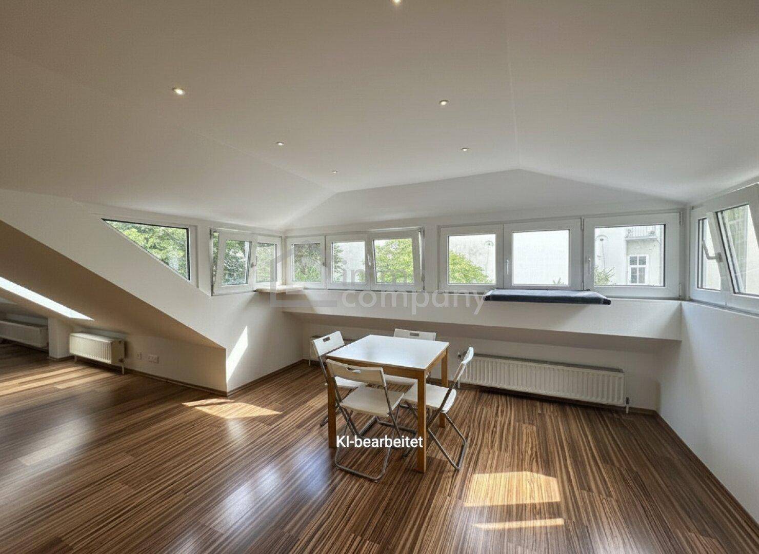 Lichtdurchfluteter Raum im Dachgeschoss mit Holzboden, vielen Fenstern und einem Esstisch.