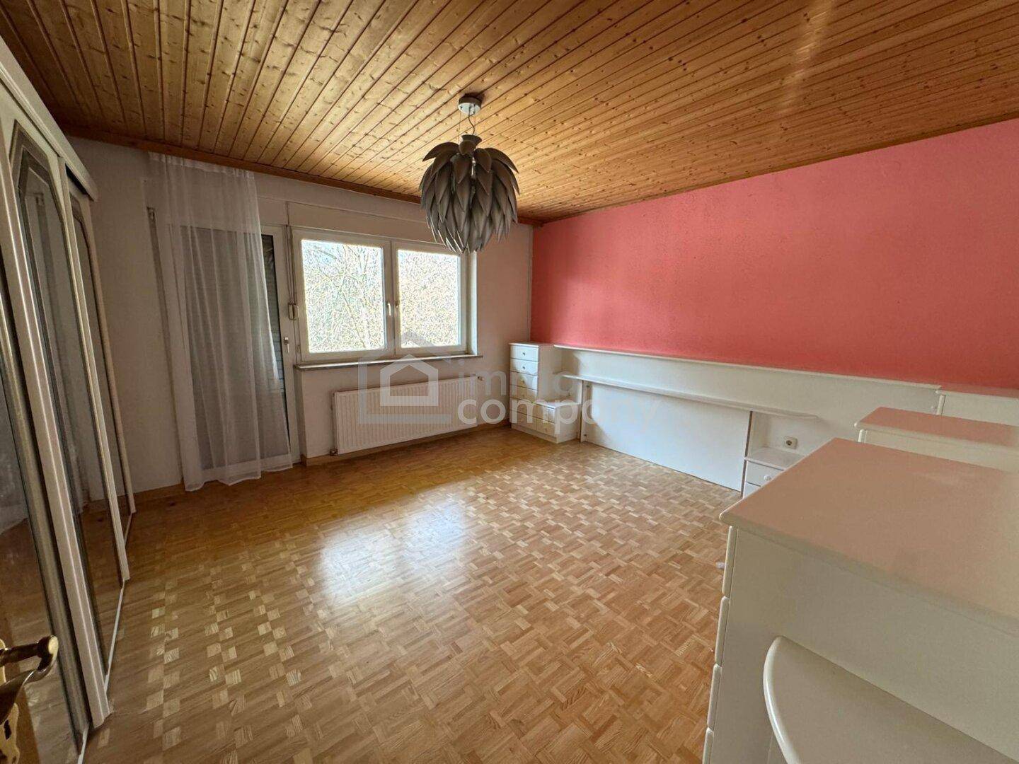Leeres Schlafzimmer mit Parkettboden, Holzdecke und rosa Akzentwand.
