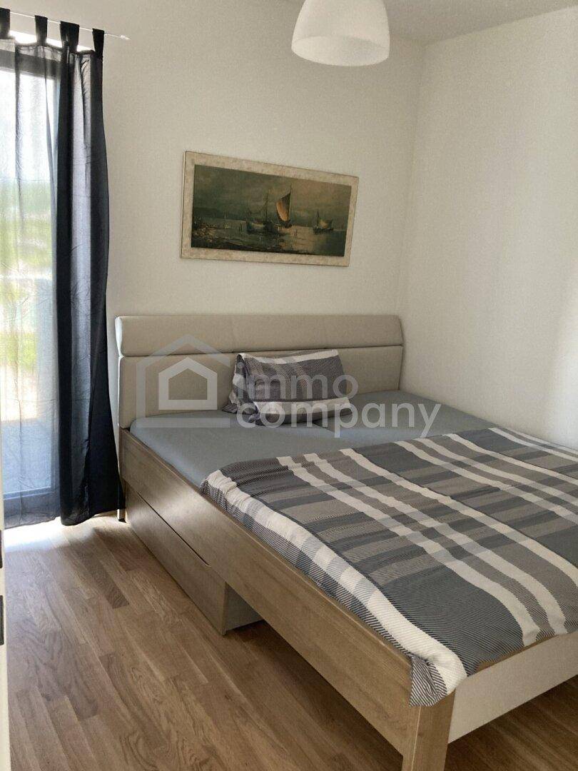Schlafzimmer mit einem bequemen Bett, Holzboden und dunklen Vorhängen am Fenster.
