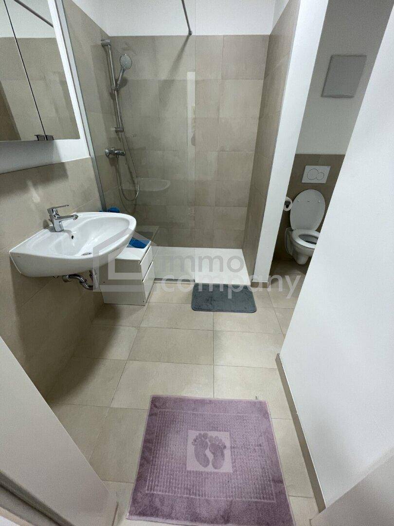 Modernes Badezimmer mit ebenerdiger Dusche, Waschbecken und separatem WC-Bereich.