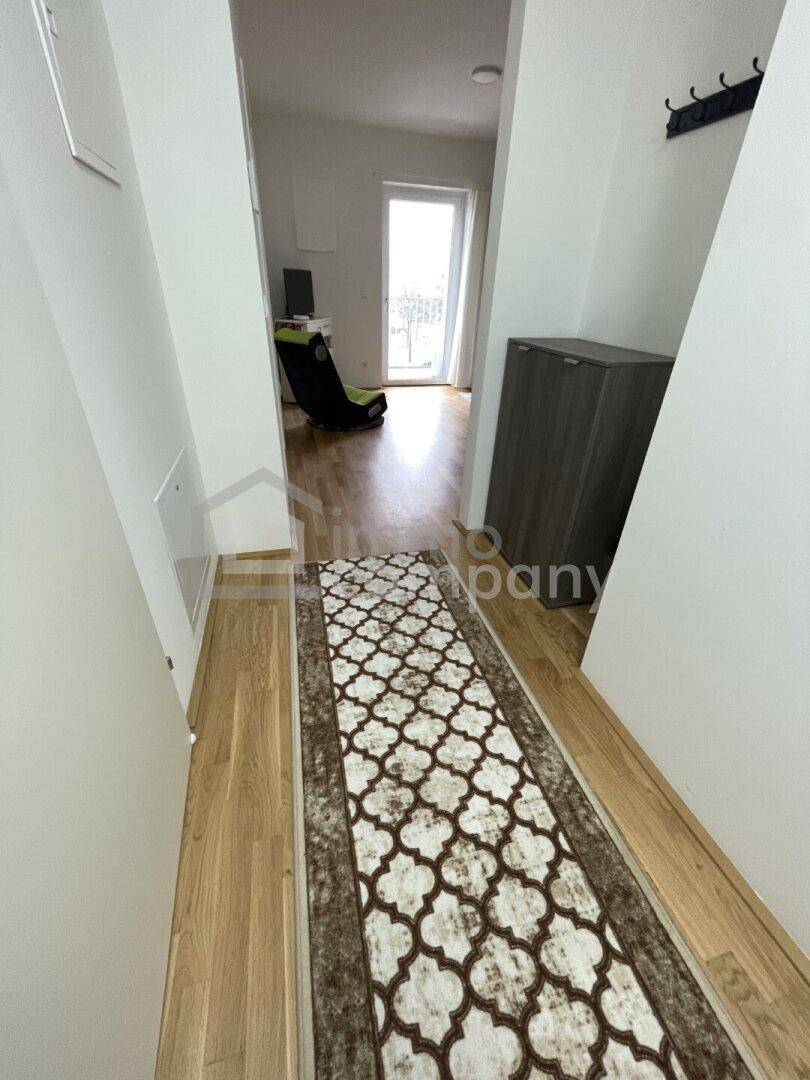 Heller Flur mit gemustertem Teppichläufer und Holzfußboden, der zu den Wohnbereichen führt.