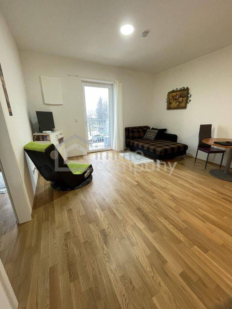 Gemütliches Wohnzimmer mit Sofa, Esstisch und Zugang zu einem kleinen Balkon.