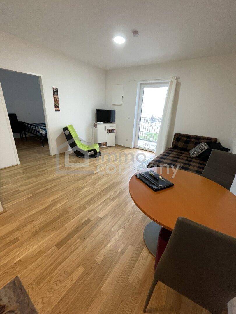 Heller Wohnbereich mit Sitzgelegenheiten und Balkonzugang, ideal für entspannte Stunden.