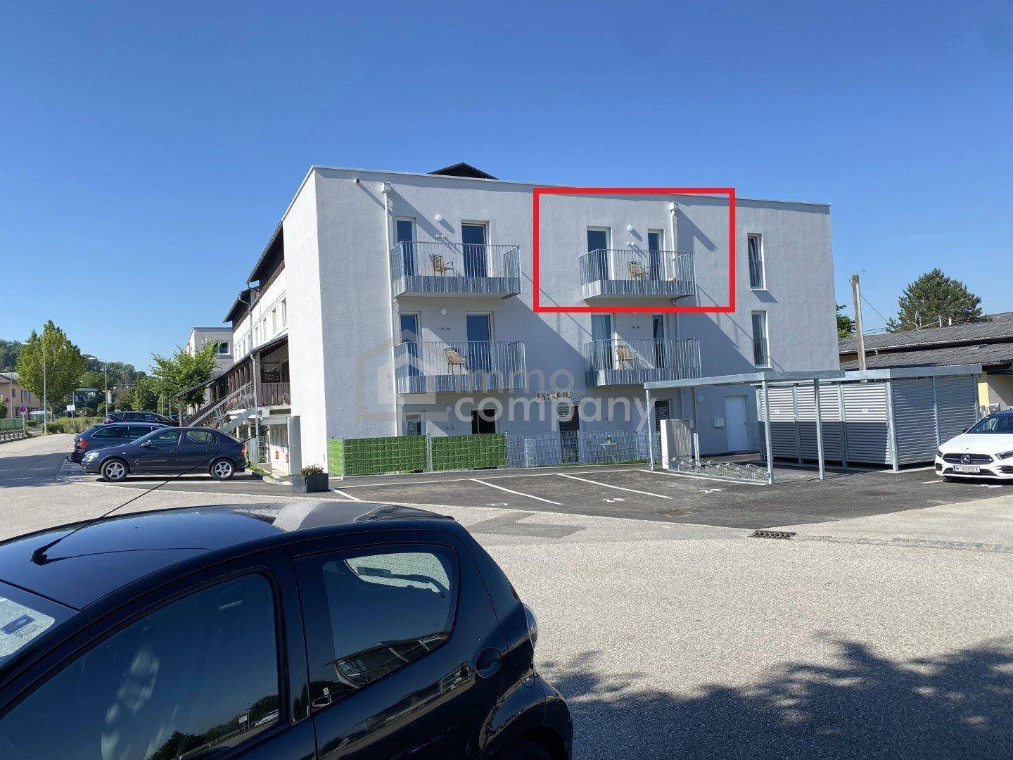 Moderne Wohnanlage mit mehreren Balkonen und Parkplätzen im Freien.