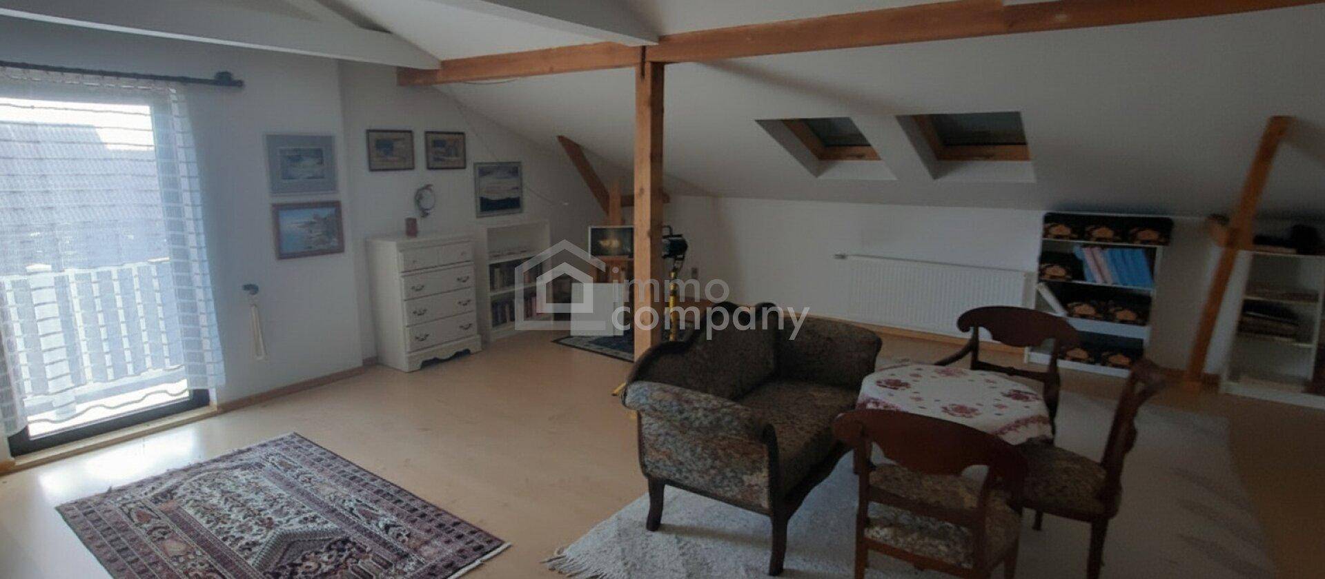 Gemütlicher Wohnbereich im Dachgeschoss mit sichtbaren Holzbalken und schrägen Decken.