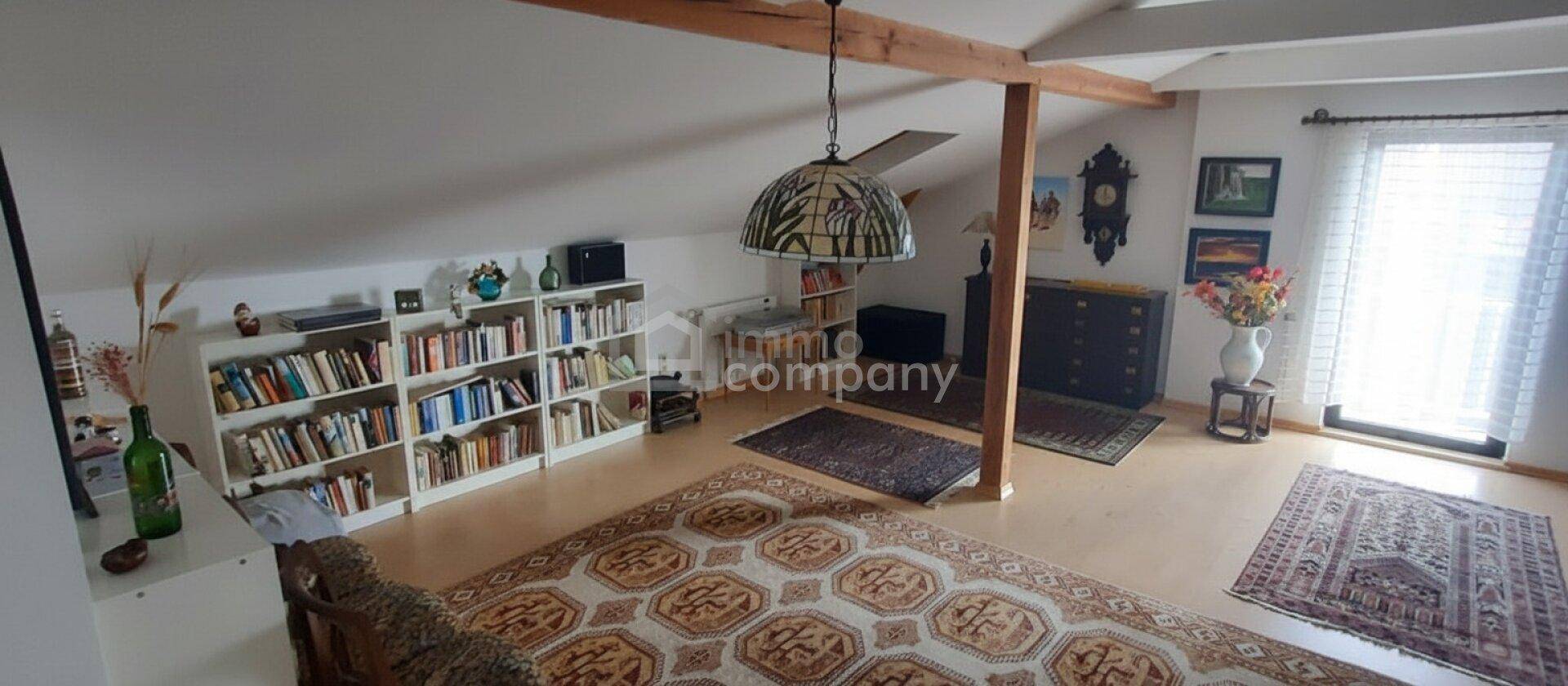 Heller Wohnraum im Dachgeschoss mit umfangreichen Bücherregalen und einem großen Orientteppich.