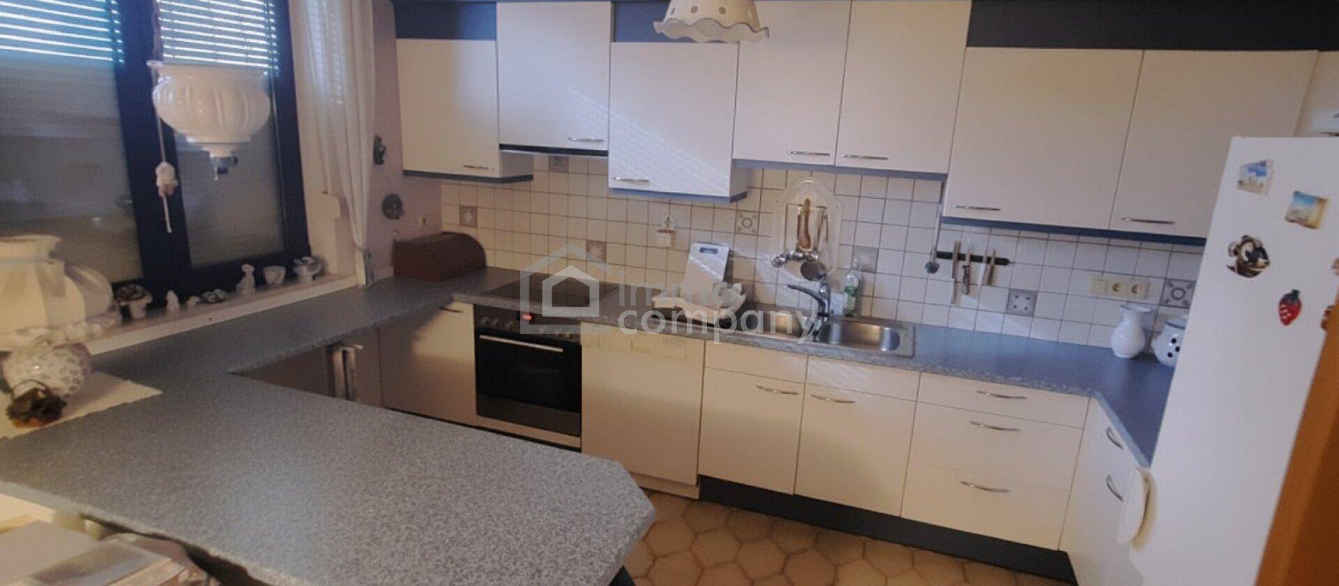 Funktionale Küche mit weißen Schränken, gefliestem Spritzschutz und Fenster über der Spüle.