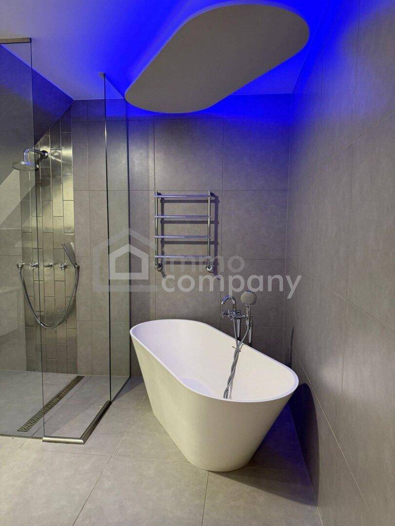 Modernes Badezimmer mit freistehender Badewanne, begehbarer Dusche und blauer Deckenbeleuchtung.