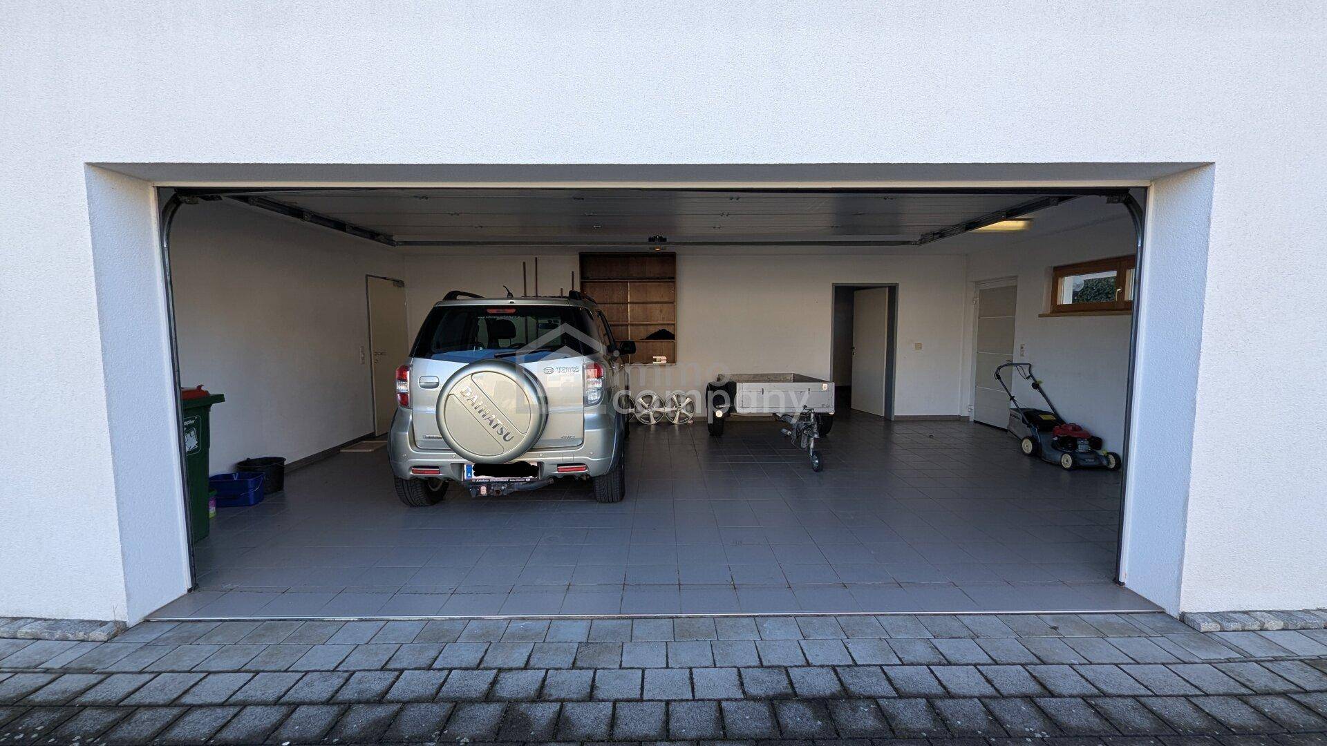 Geräumige Doppelgarage mit Fliesenboden, einem Auto und Gartengeräten.