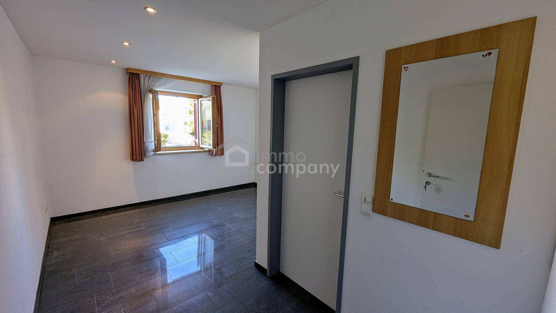 Leeres Zimmer mit dunklem Fliesenboden und Fenster, das Tageslicht spendet.