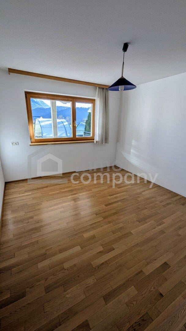 Helles Zimmer mit Holzboden und Fenster, das viel Tageslicht hereinlässt.