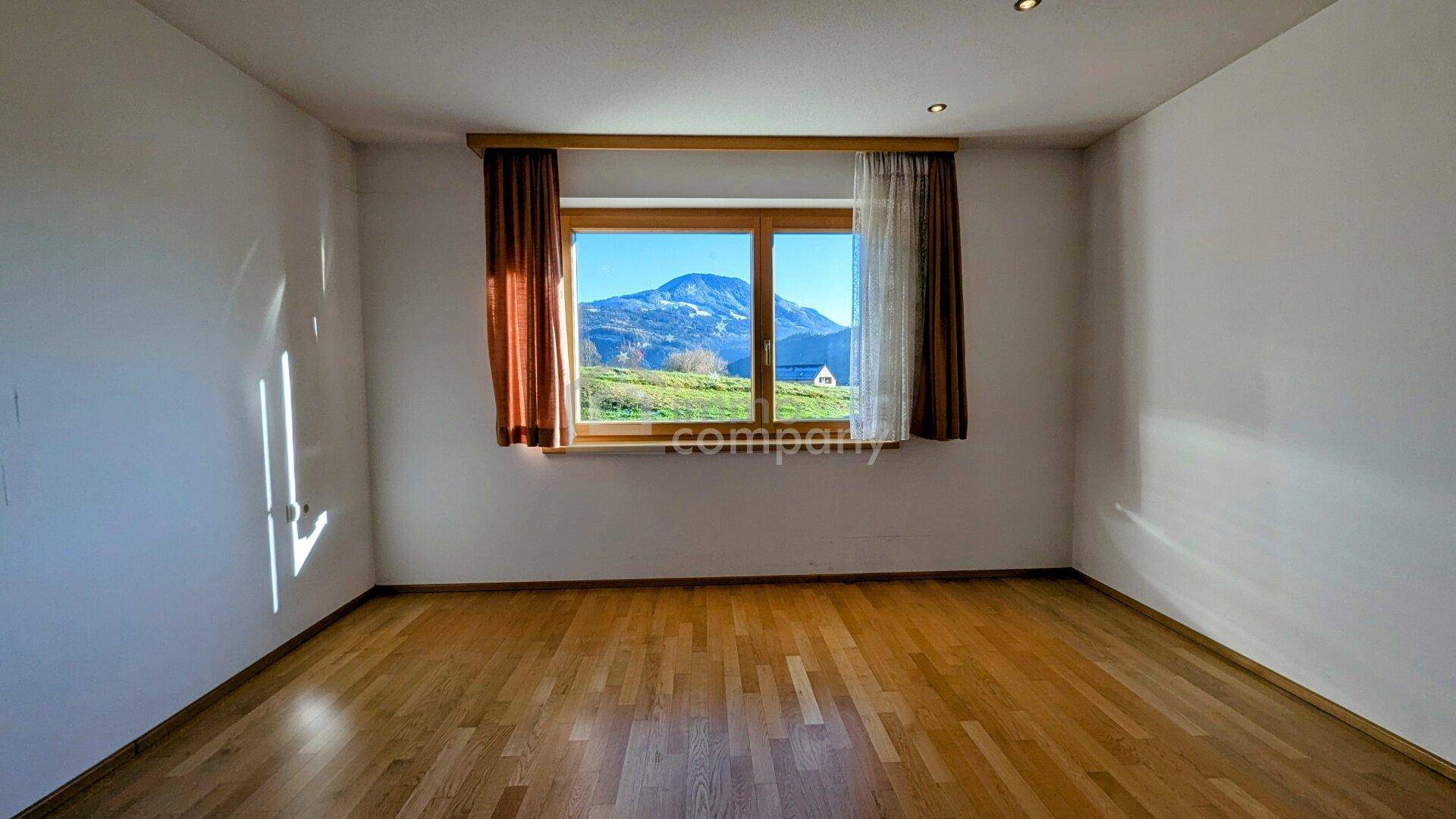 Helles Schlafzimmer mit Holzboden und einem Fenster mit Bergblick.