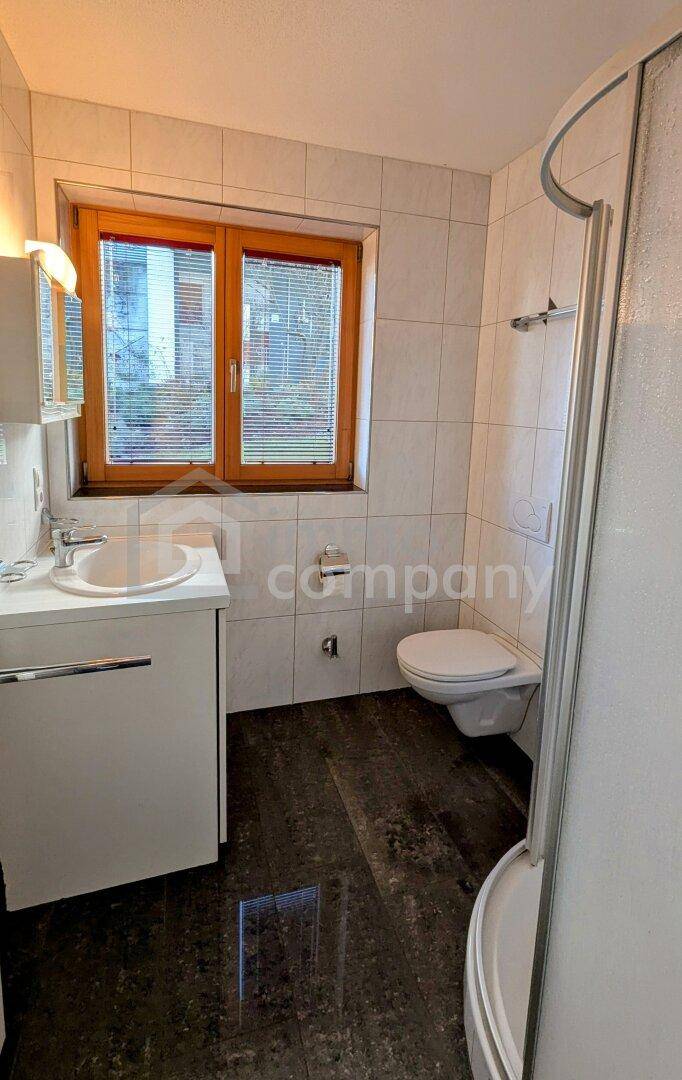 Kleines Badezimmer mit Dusche, WC, Waschbecken und Fenster.