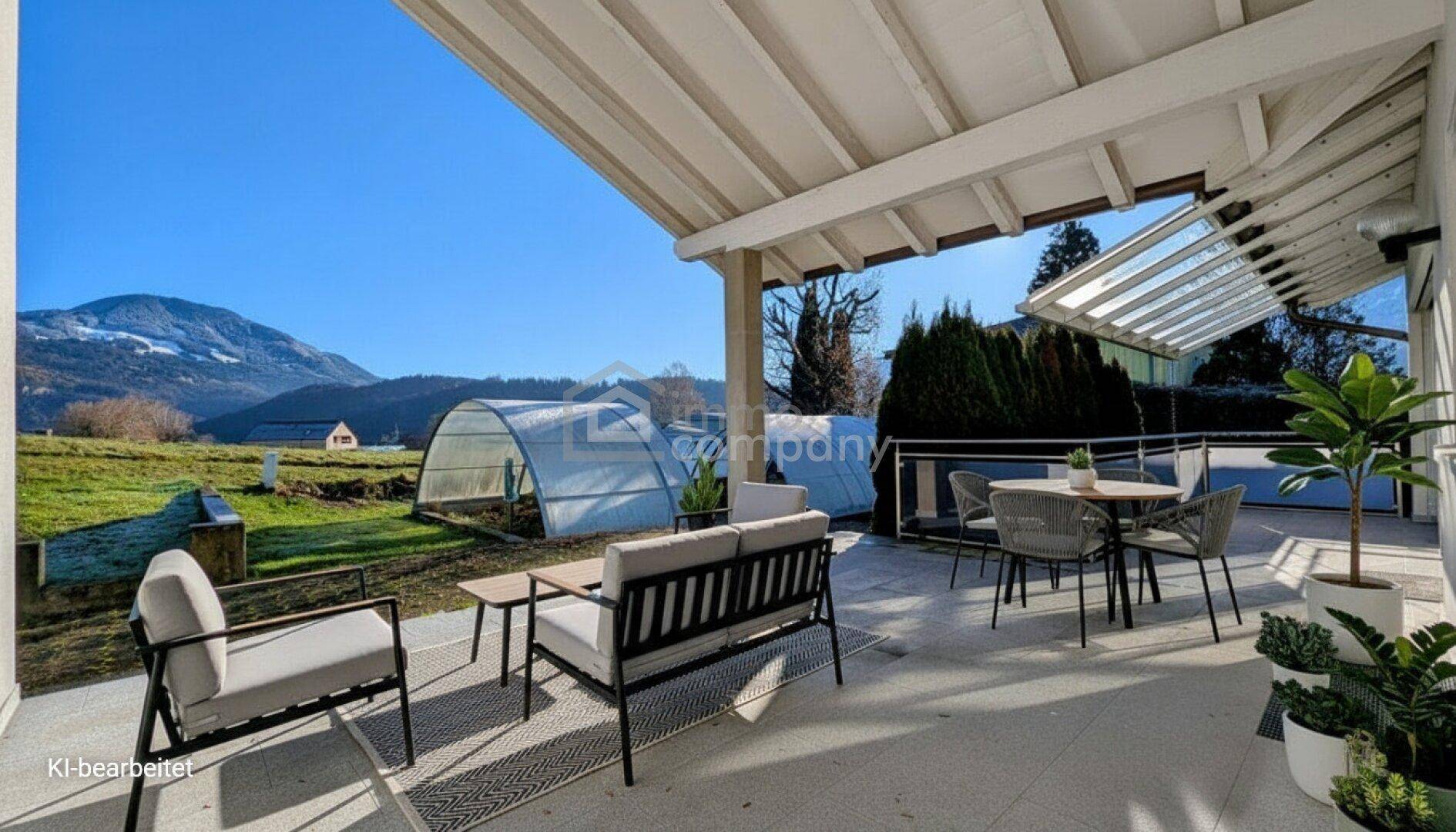 Möblierte überdachte Terrasse mit Blick auf die umliegende Landschaft und Berge.