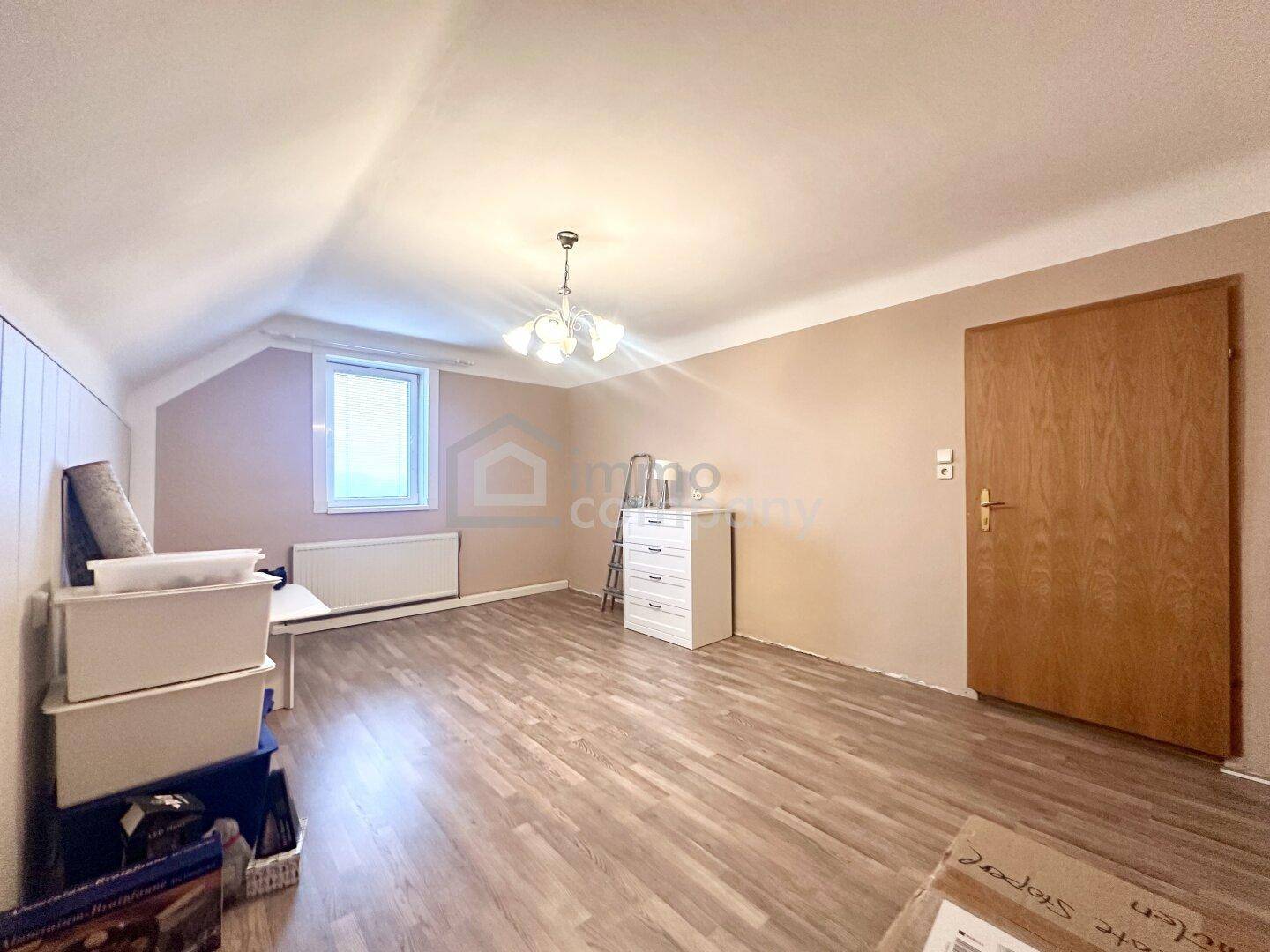 Helles Zimmer im Dachgeschoss mit Laminatboden, schrägen Wänden und einem Fenster.