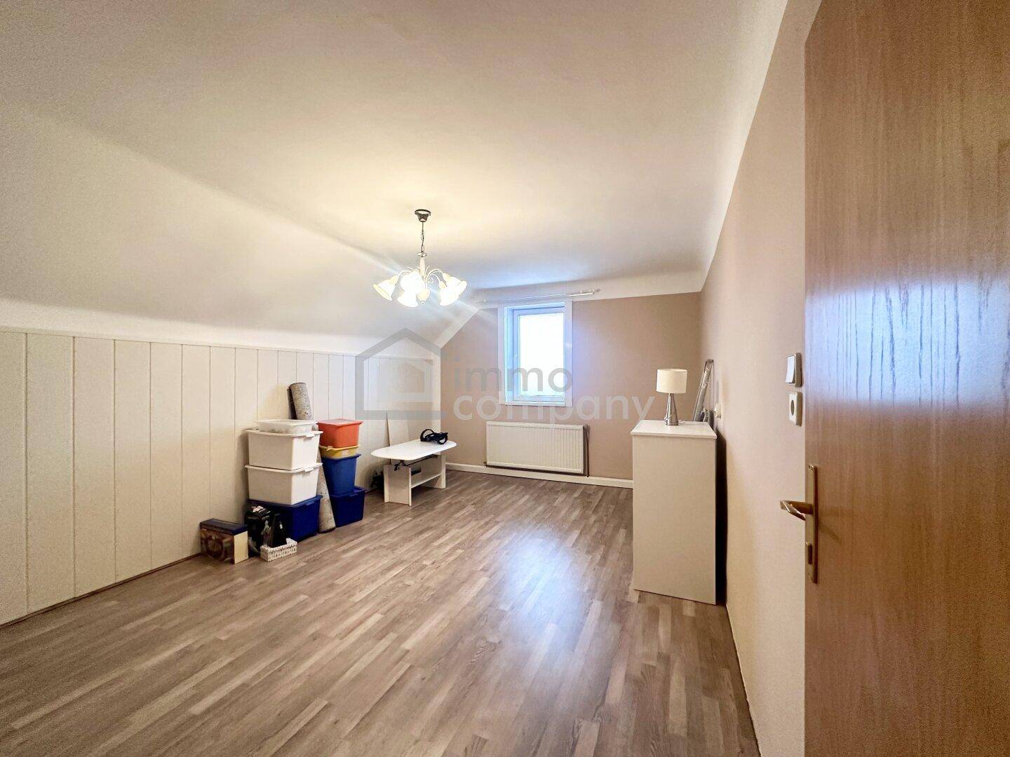 Geräumiges Dachzimmer mit Laminatboden, schrägen Wänden und einfacher Einrichtung.