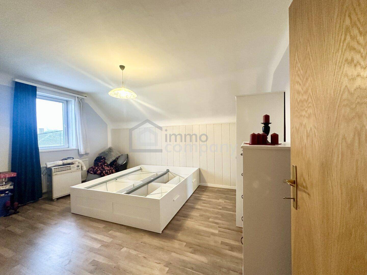 Schlafzimmer im Dachgeschoss mit Laminatboden, Fenster und einem Bettgestell mit Stauraum.