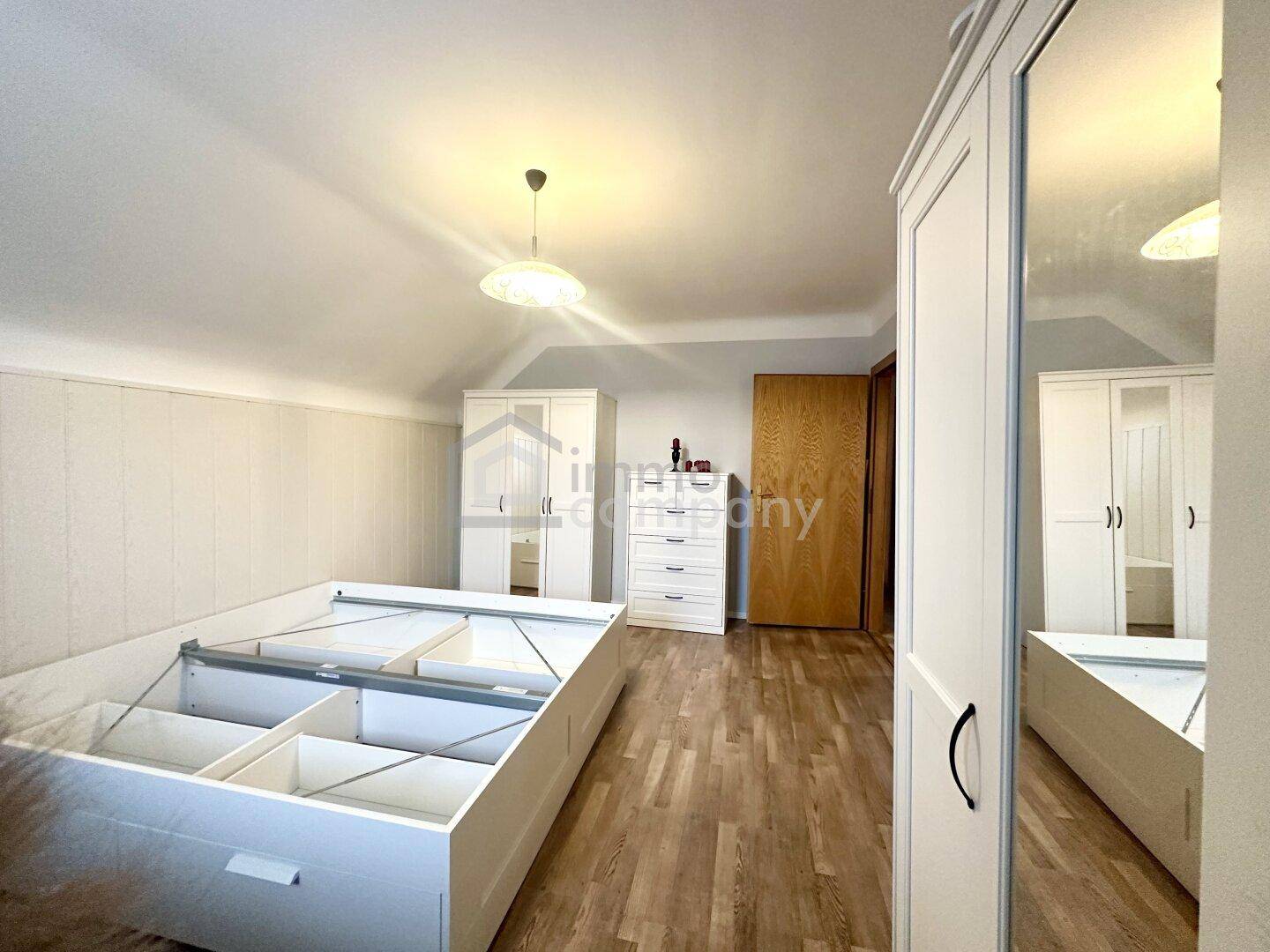 Helles Schlafzimmer im Dachgeschoss mit Laminatboden, weißem Mobiliar und Stauraum.